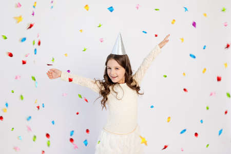 A cute little girl with a cap on a white isolated background with a serpentine dancing and rejoicing. Space for text. Little girl celebrates birthday, holiday conceptの写真素材