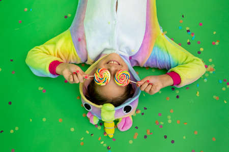 little girls in bright costumes lie on a green isolated background with a streamer in bright unicorn costumes. Space for text. The concept of a holiday, Birthday and salesの写真素材