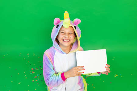a little girl on a green isolated background in a bright suit holding a white sheet of paper. Space for text. The concept of a holiday, Birthday and salesの写真素材