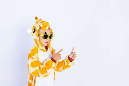 a cheerful boy in a bright orange giraffe costume points with his fingers on a white isolated background, a place for textの写真素材