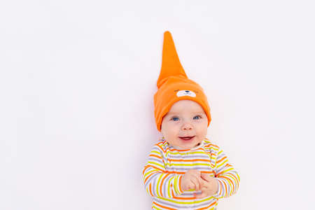 small smiling baby girl 6 months old lying on a white isolated background in an orange cap cap, space for textの写真素材