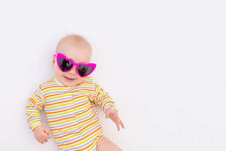 small smiling baby girl 6 months old lying on a white isolated background in bright sunglasses, space for textの写真素材