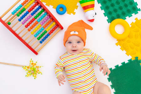 small smiling baby girl 6 months old lies on a white isolated background among toys, space for textの写真素材