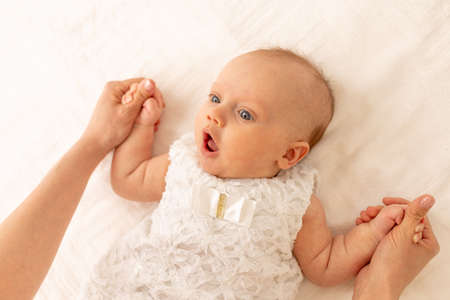 a mother holds the hands of a surprised baby on a white bedの写真素材