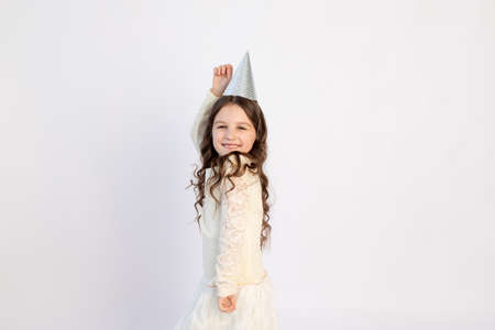 A cute little girl with a cap on a white isolated background is dancing and rejoicing. Space for text. Little girl celebrates birthday, holiday conceptの写真素材