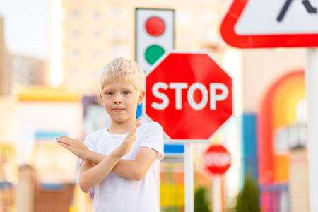 a child stands at a STOP sign and holds his hands in a cross, traffic rules for childrenの写真素材
