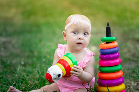 baby girl 10 months old sitting on the grass in the summer and playing pyramid, early development of children, outdoor gamesの写真素材