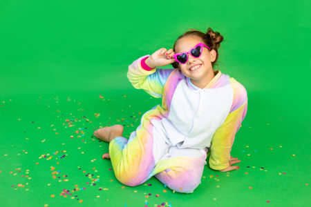 a little girl is sitting on a green isolated background with a streamer in a bright suit and glasses. Space for text. The concept of a holiday, Birthday and salesの写真素材