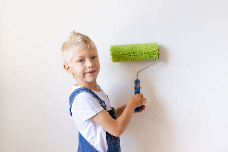 child boy Builder paints white walls with a roller in the apartment, the child makes repairs at homeの写真素材
