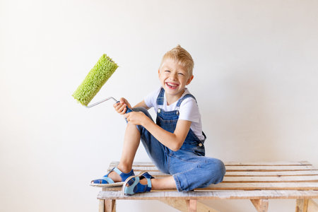a smiling child Builder sits on a construction ladder in an apartment with white walls and holds a...