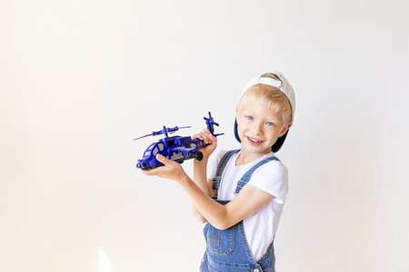 kid boy in blue jeans is playing with a helicopter on background white isolated background, place...