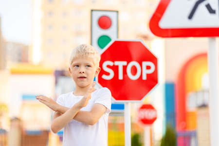 a child stands at a STOP sign and holds his hands in a cross, traffic rules for childrenの写真素材