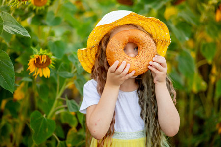 a little girl looks through a bagel in a field of sunflowers in summer
