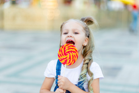 a baby girl stands in an amusement Park and eats a large Lollipopの写真素材