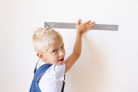 child Builder measures a white wall with a construction ruler, space for text, construction and repair conceptの写真素材