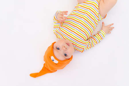 small smiling baby girl 6 months old lying on a white isolated background in an orange cap cap, space for textの写真素材