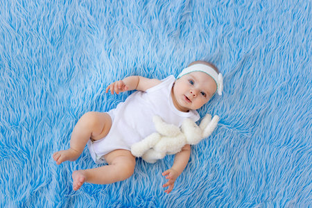 a smiling child in a white bodysuit lies on a blue fur background with a toy.