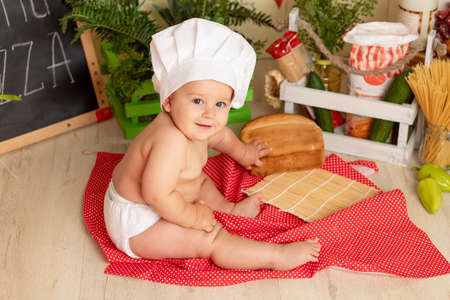 happy little child in a chef's hat sitting in the kitchen with breadの写真素材