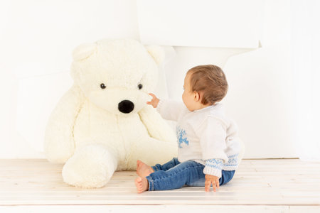 a small child six months old in a knitted warm jacket and blue jeans is sitting at home with a large...