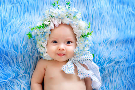 baby in a flower hat on a blue background, beautiful photo of a little girl six months old with flowersの写真素材