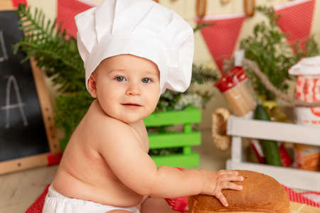 happy little child in a chef's hat sitting in the kitchen with breadの写真素材