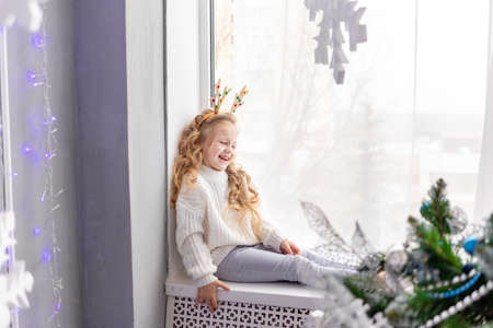 happy baby girl sitting at the window of the house before the new yearの写真素材