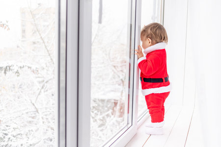 child in Santa suit on the sill of the window, the concept of new year and Christmas