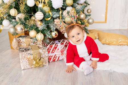 a child in a Santa costume sits at the Christmas tree with gifts, the concept of new year and Christmasの写真素材