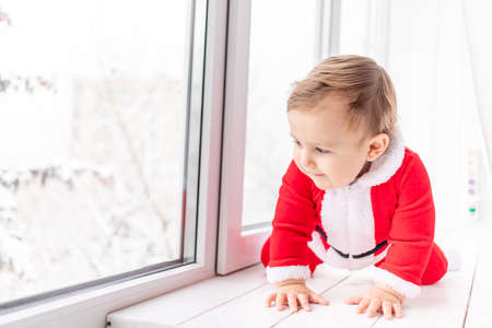 child in Santa suit on the sill of the window, the concept of new year and Christmasの写真素材