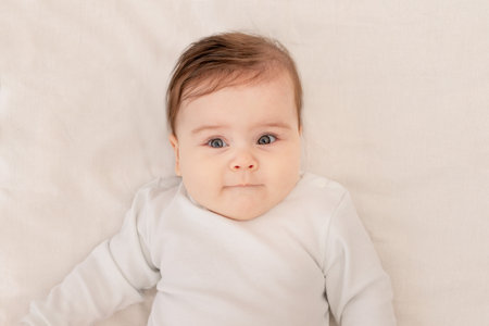 cute baby six months lying in a crib in a white bodysuitの写真素材
