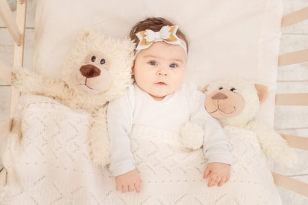 the baby is six months old in a crib in a white bodysuit with a Teddy bear