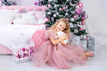 baby girl with rabbit at the Christmas tree in a beautiful pink dress, new year and Christmas conceptの写真素材