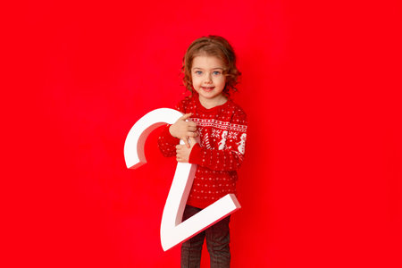 little girl holding the number two in winter clothes on a red background, space for textの写真素材