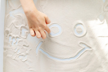 hands of a child drawing a smile on the sand