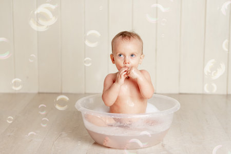 the baby bathes or washes in a basin with foam and soap bubblesの写真素材
