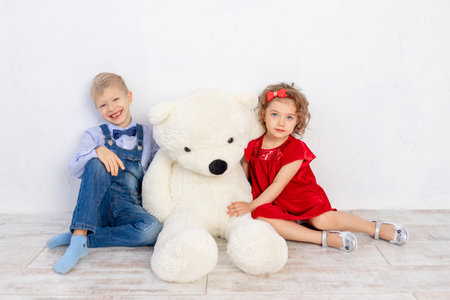 a girl with a boy sitting with a big Teddy bear, the concept of family and friendshipの写真素材
