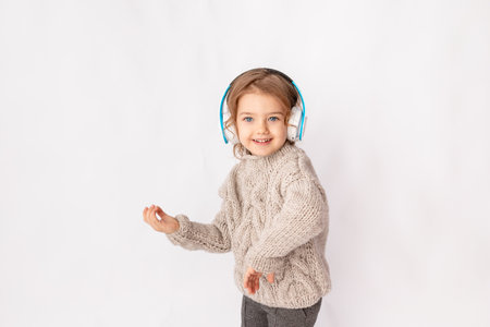 little girl with headphones on a white background listening to music and dancing, space for textの写真素材