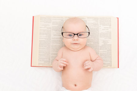 baby with glasses and a book on a light background, learning and development conceptの写真素材