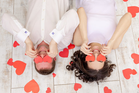 valentine's day, a couple in love lies among the hearts on the floor with their eyes closed with heartsの写真素材