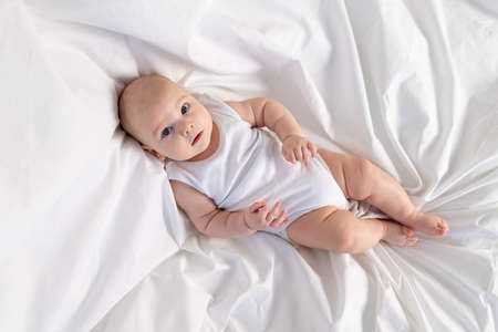 a child on a white bed in the morning. Textiles and bed linen for children. A newborn baby has woken up or is going to bedの写真素材