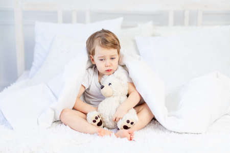 a child is sad with a teddy bear on the bed at homeの写真素材