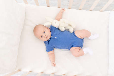 a baby boy in a crib lies on his back with a toy, a happy newborn wakes up in the morning or goes to bedの写真素材