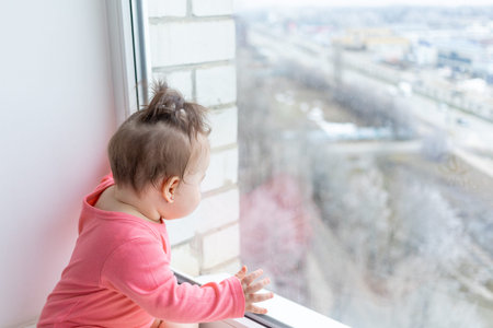 the baby sits on the window sill and looks out at the street
