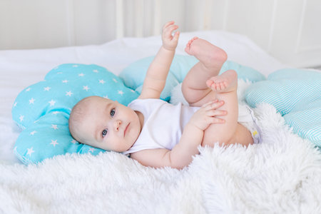 baby boy in the crib before going to bed with blue textiles playing with his feet, cute...