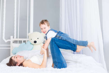 A happy, loving family. Mom and baby son play at home on the bed, have fun and laughの写真素材