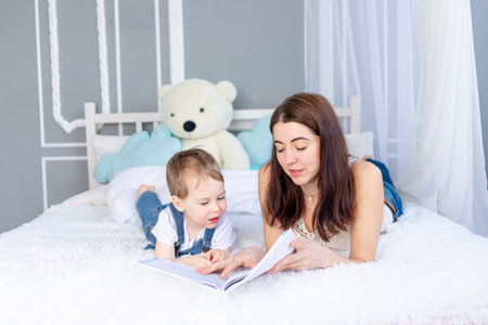 mom reads a book to the child or teaches him at home on the bed Happy loving family. Mom and son