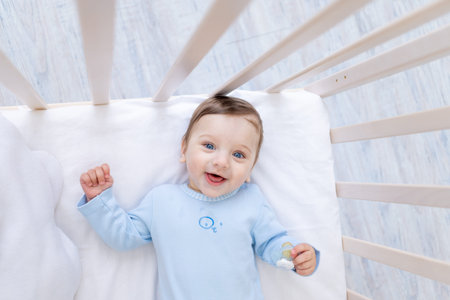 happy smiling baby boy in crib in blue bodysuit, cute joyful little baby in bedroom
