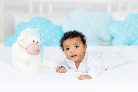 African-American little baby in a crib in the bedroom lying on her tummy with a stuffed toy