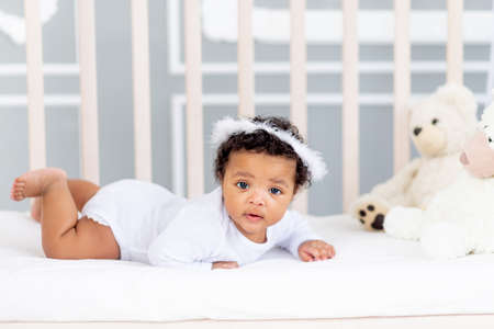 cute African-American little baby lying in bed for sleeping with angel headbandの写真素材