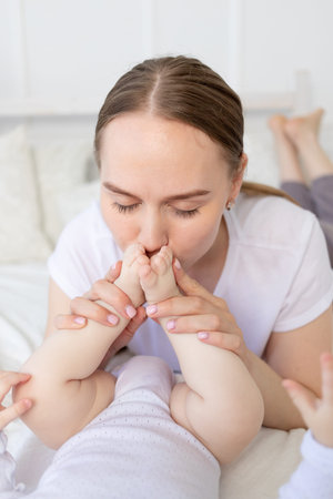 mother kisses baby's feet and sniffs them on the bed at home, happy motherhood
